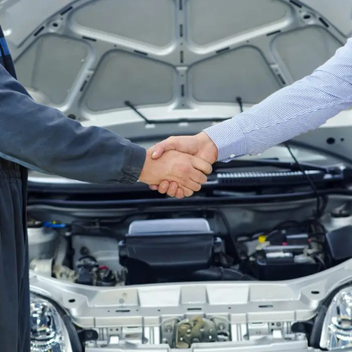 Mechanic shaking hands with customer after car repair with open hood